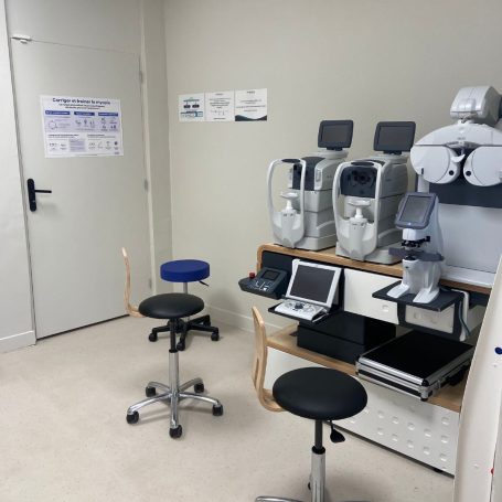 Salle d'examen avec deux chaises, un appareil médical et des équipements sur une table.