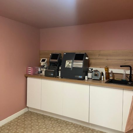 Coin cuisine avec des machines à café et un évier, murs en rose pâle.