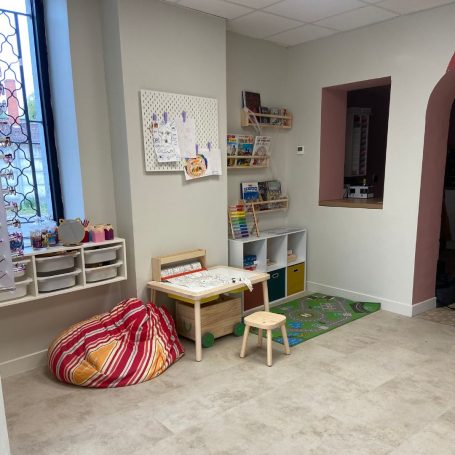 Salle de jeux avec des rangements, un tapis vert et un coin lecture confortable.